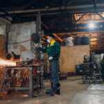 Workers working with metal construction on plant. Metal processing with big angle grinder disk saw and welder welding. Sparks in metalworking at factory