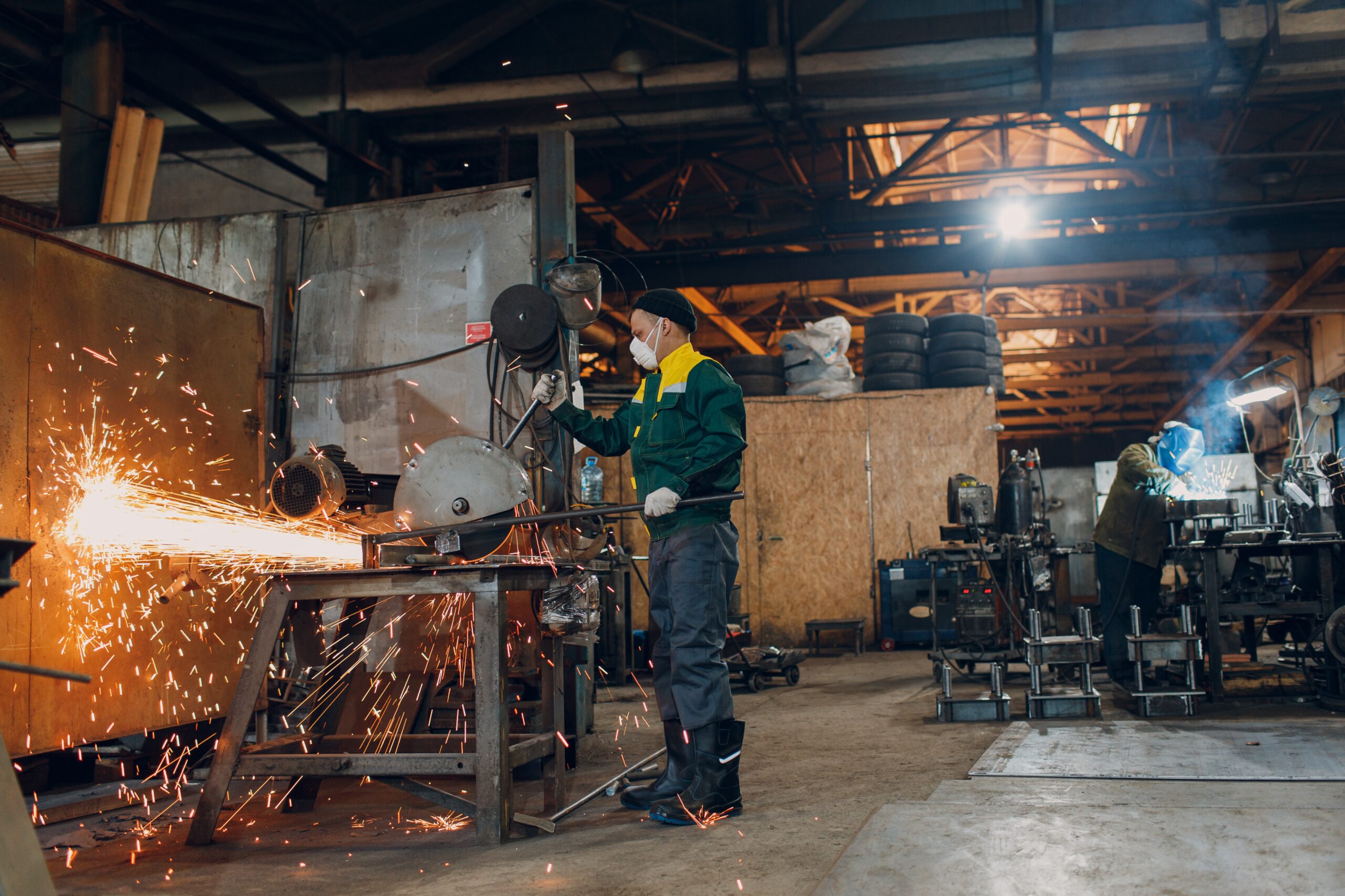 Workers working with metal construction on plant. Metal processing with big angle grinder disk saw and welder welding. Sparks in metalworking at factory