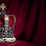 Royal golden crown with jewels on pillow on pink red background.